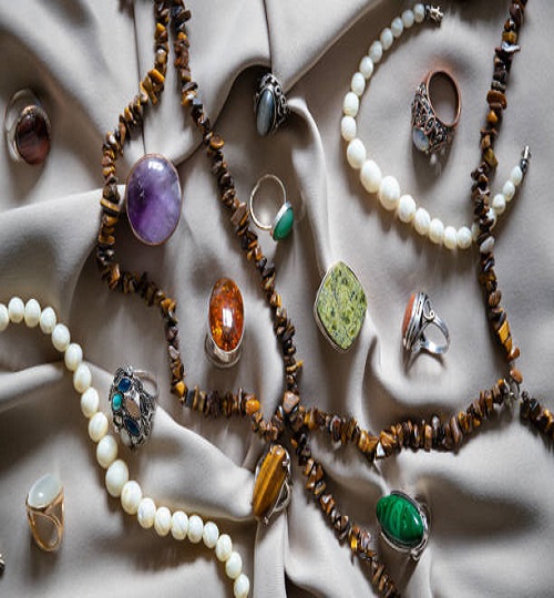 Many different silver rings and necklace with various natural gemstones over  background.