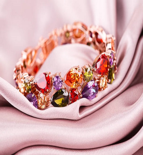 Stylish bracelet with colorful stones on fabric background.