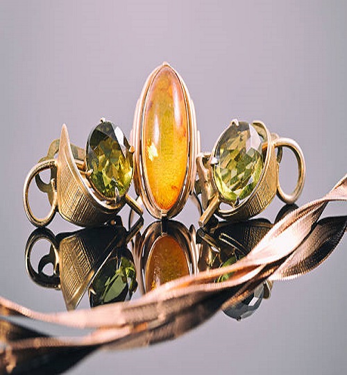 Old gold earrings with green stones and a ring with amber in the background of a gold chain